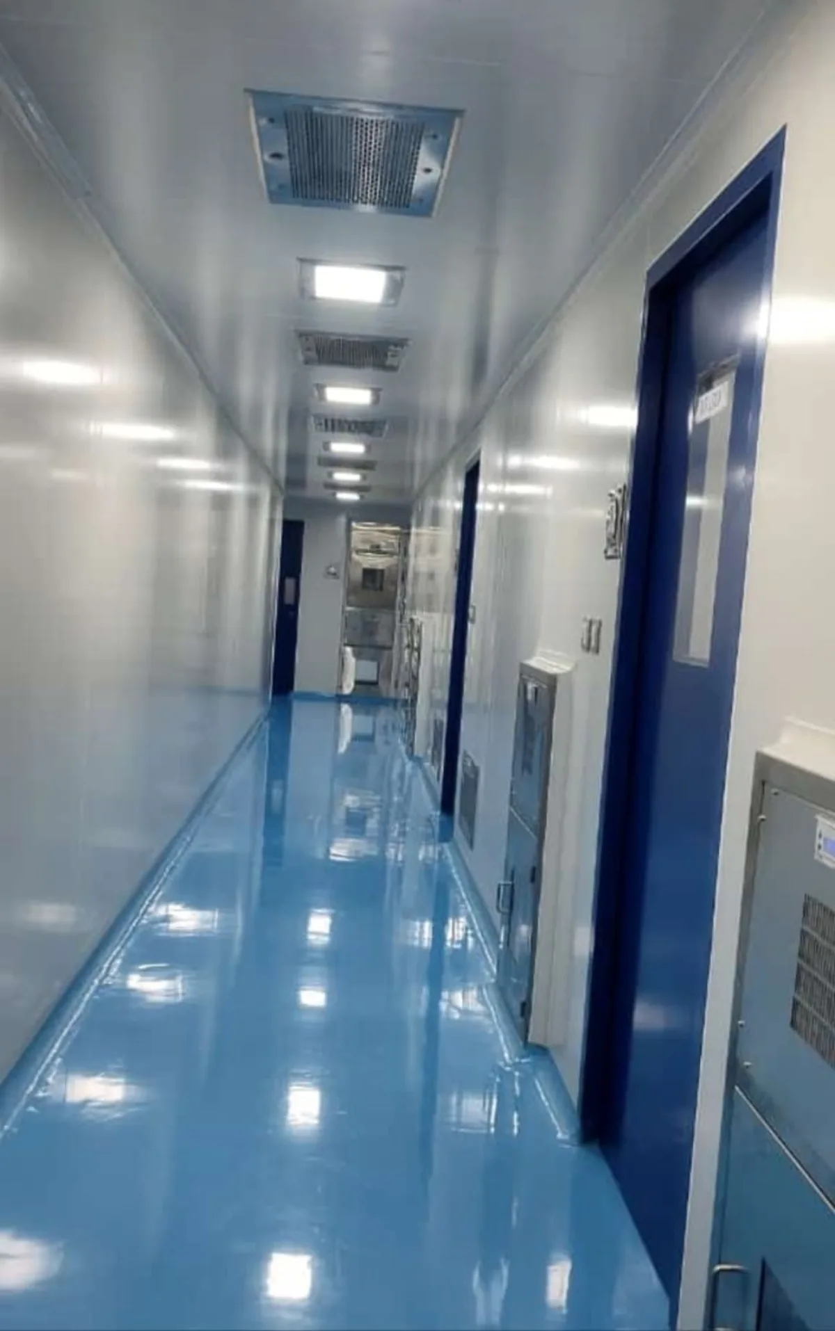 Cleanroom corridor with blue epoxy floor, ceiling-mounted HEPA terminal filter units and controlled doors with vision panels
